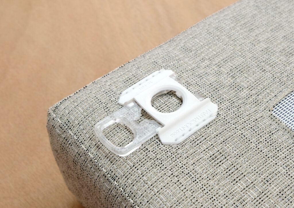 FAS011 - Best Award Textile 1-0-2344-0-1652 A white and clear plastic bread bag clip, designed by a freelance industrial designer, rests on a light grey, textured fabric surface atop a wooden table.