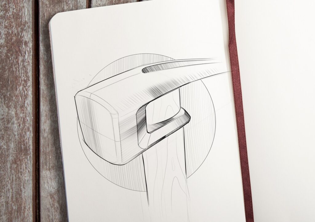 Hammer Head A sketch by Evan Thomas of a sledgehammer head with a wooden handle, drawn in black ink on white paper in a notebook, rests on a wooden surface with a brown ribbon bookmark visible—showcasing Industrial Design Auckland flair.
