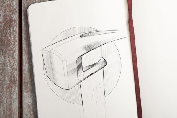 Hammer Head A sketch by Evan Thomas of a sledgehammer head with a wooden handle, drawn in black ink on white paper in a notebook, rests on a wooden surface with a brown ribbon bookmark visible—showcasing Industrial Design Auckland flair.